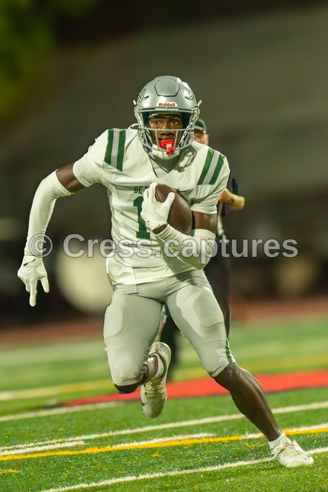 Football receiver in a white uniform and silver helmet runs upfield carrying the ball