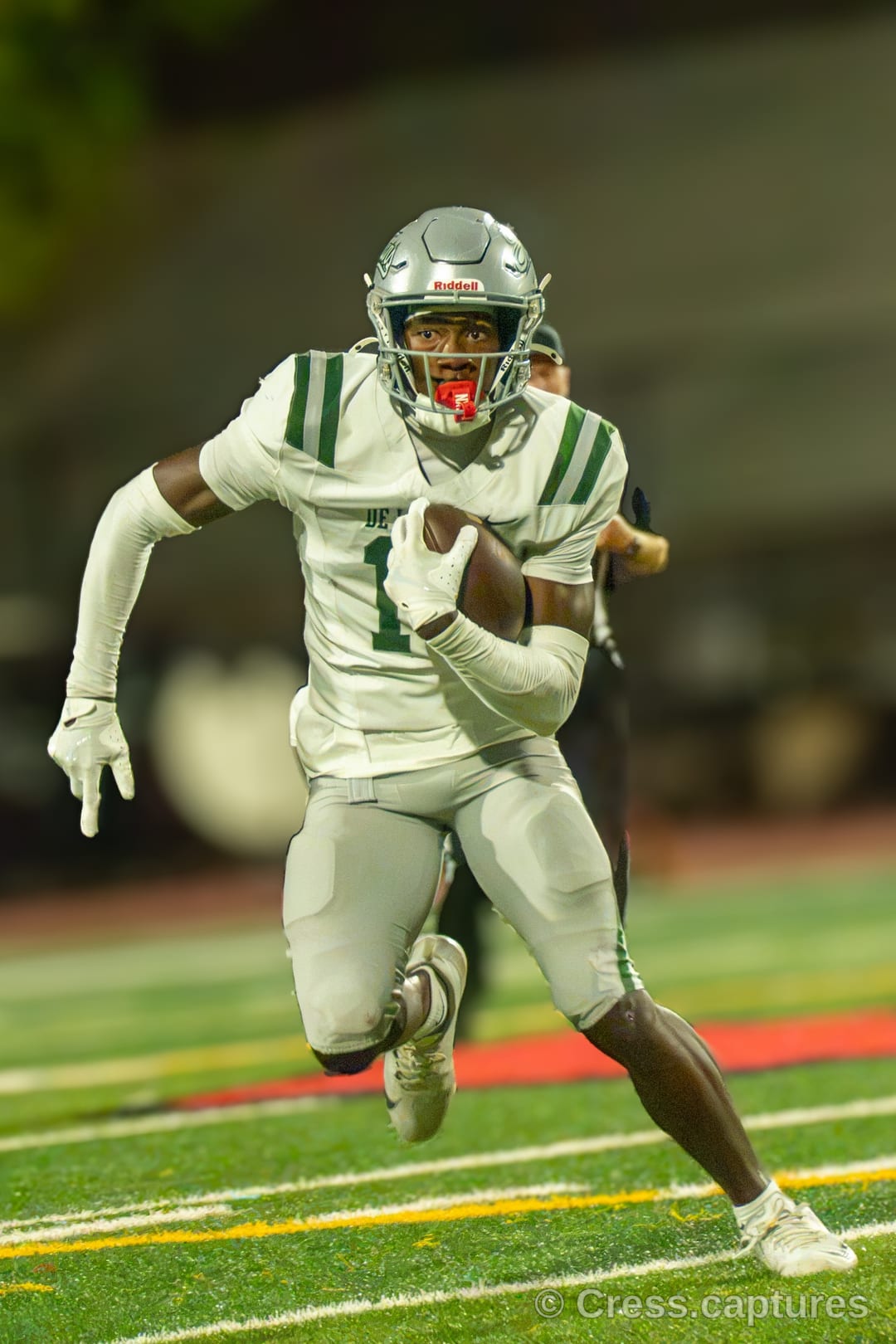 Football receiver in a white uniform and silver helmet runs upfield carrying the ball